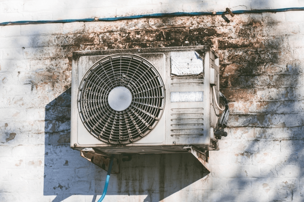 An AC compressor installed on a dirty wall.